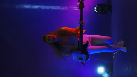 Vertical-video-crazy-women-rock-musician-playing-guitar-in-the-Studio-in-the-light-of-spotlights-and-smoke-dancing-and-jumping-in-the-Studio